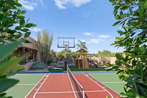 Ein Basketballfeld mit Netz, eine Holzspielkonstruktion und ein Schwimmbecken im Hintergrund.