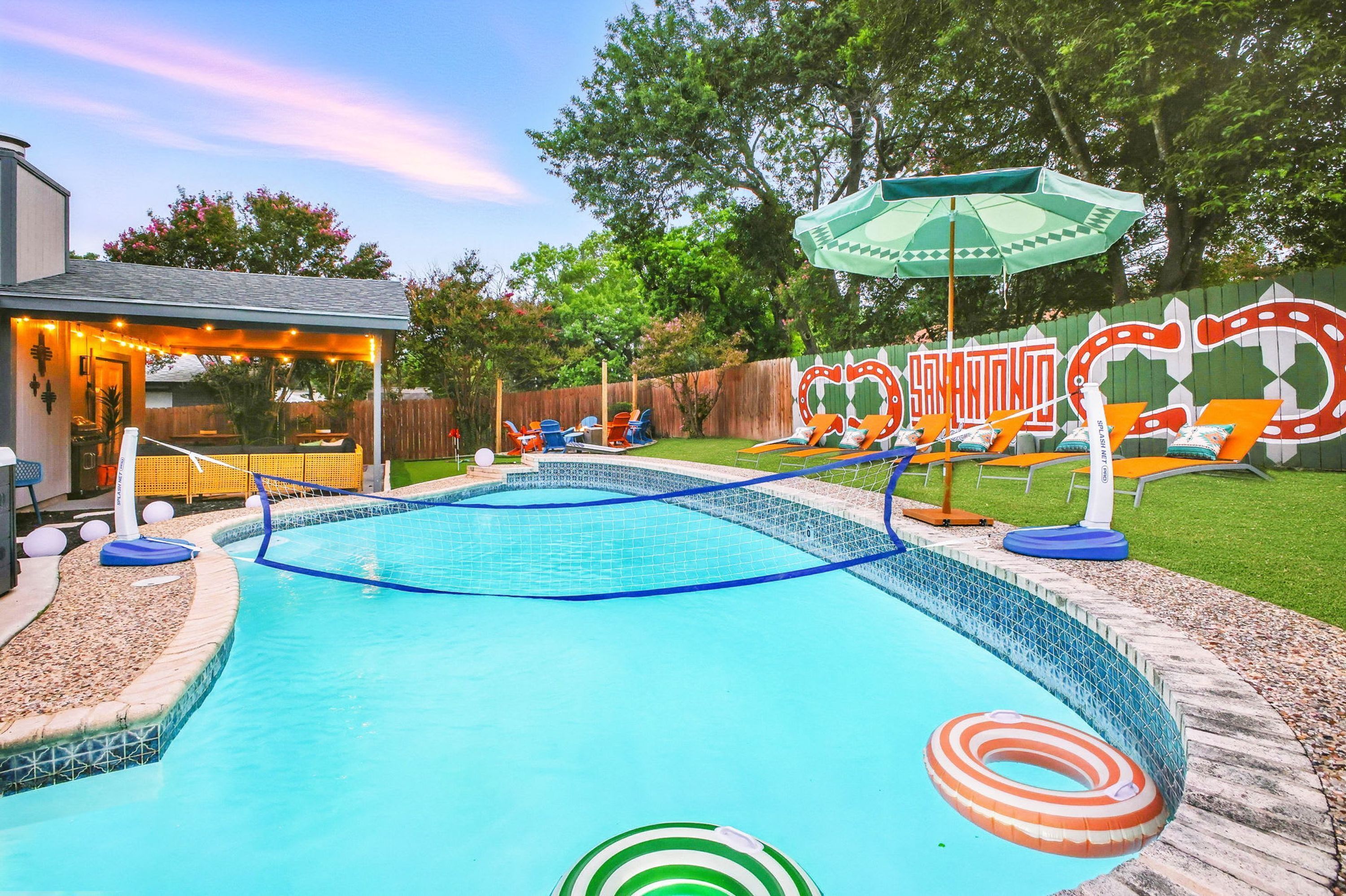 A backyard with a swimming pool, lounge chairs, and a covered patio area.
