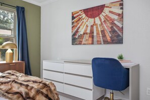 A room with a bed, a desk with a chair, a dresser, a window with curtains, and a wall-mounted artwork. - Soak Sizzle Score Pool Games More (San Antonio)