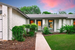 A single-story house with a brick exterior, a front door, and a small front yard with shrubs and a lawn. - Soak Sizzle Score Pool Games More (San Antonio)