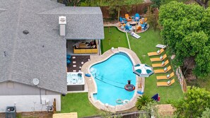 A backyard with a swimming pool, lounge chairs, and a fire pit area. - Soak Sizzle Score Pool Games More (San Antonio)