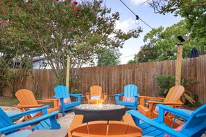 A backyard with a fire pit surrounded by colorful Adirondack chairs. - Soak Sizzle Score Pool Games More (San Antonio)