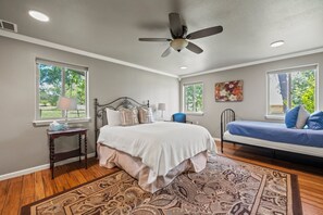 Ein Schlafzimmer mit einem Bett, einem Schreibtisch, einem Stuhl, einem Deckenventilator und einem Fenster.