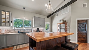 A modern kitchen with a central island, grey cabinets, and a wooden countertop. - The Live Oak Pickleball-hot Tub-dog Friendly (Fredericksburg)