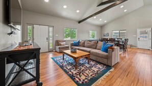 A spacious living area with a wooden floor, a sofa set, a coffee table, and a dining area with chairs. - The Live Oak Pickleball-hot Tub-dog Friendly (Fredericksburg)