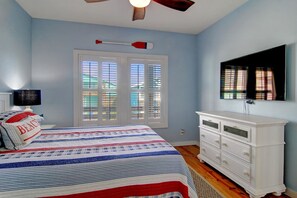 A bedroom with a bed, a dresser, a ceiling fan, and a window with blinds. - Salty Pelican - Family Friendly Community Pool (Port Aransas)