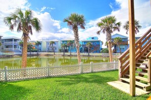 A waterfront property with a pool, palm trees, and a wooden staircase. - Salty Pelican - Family Friendly Community Pool (Port Aransas)