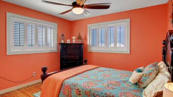 A bedroom with a bed, dresser, and two windows with blinds.