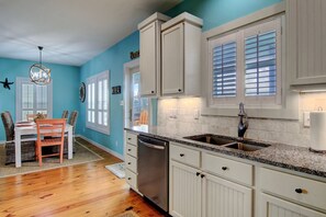 A kitchen with white cabinets, a granite countertop, and a stainless steel sink. - Salty Pelican - Family Friendly Community Pool (Port Aransas)