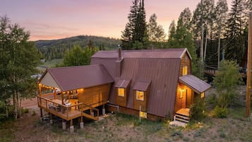 Eine Holzhütte mit Terrasse und großer Veranda, umgeben von Bäumen und einer hügeligen Landschaft.