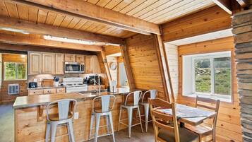 Interior de una cabaña con cocina, comedor y ventana con vistas al exterior.
