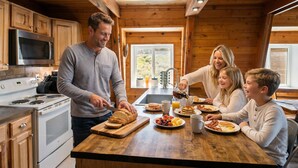 Une famille prépare le petit-déjeuner dans la cuisine de son chalet, qui est équipée d’une cuisinière moderne, de meubles en bois et d’une grande fenêtre.