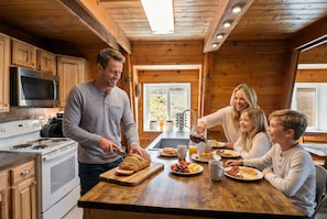 A family in a cabin kitchen preparing breakfast with a modern stove, wooden cabinets, and a large window. - Ski-lee Retreat Ski Hike Explore Sleeps 10 (Brian Head)