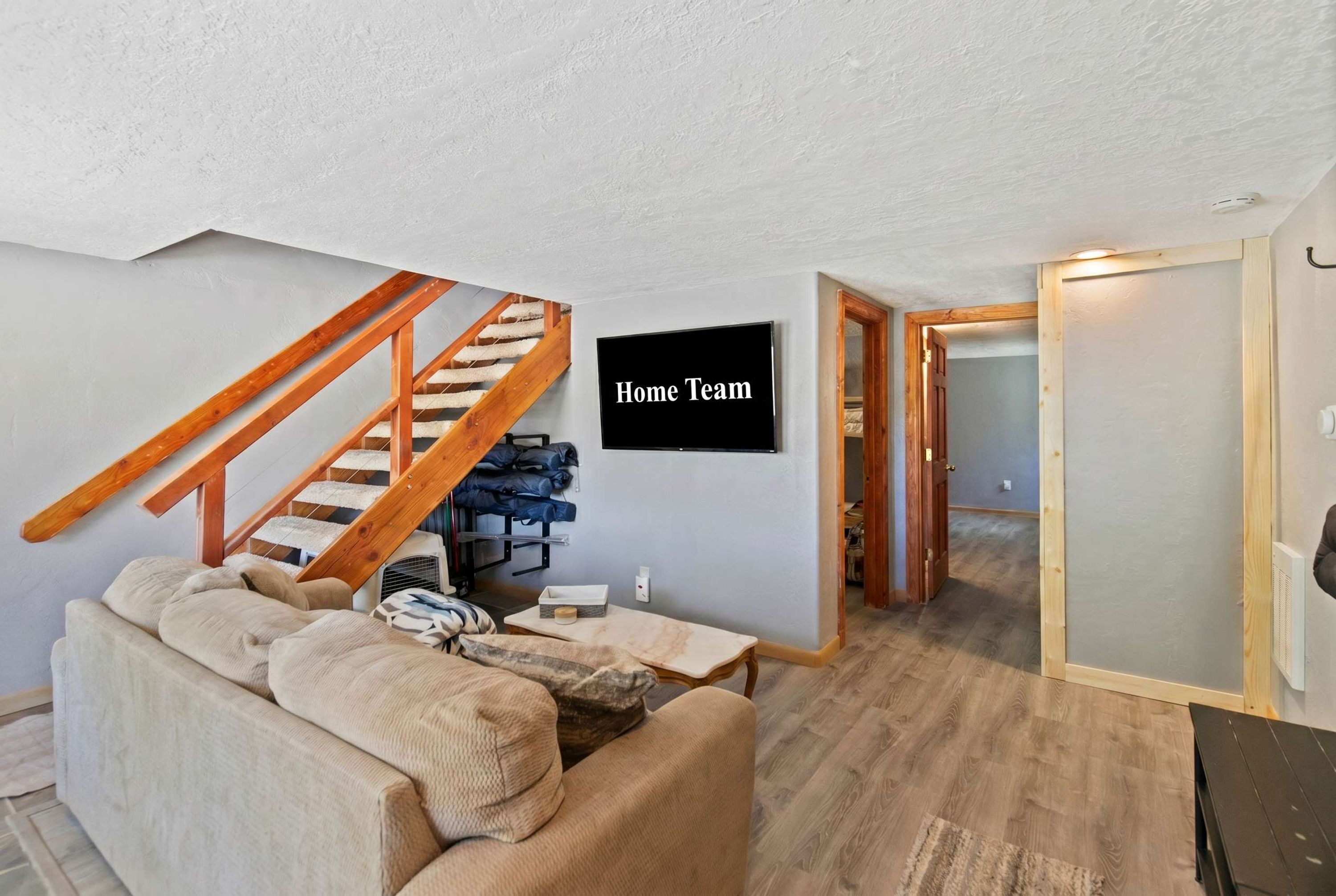 A living room with a staircase, a sofa, a coffee table, and a TV mounted on the wall.