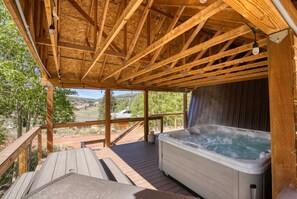 Una terraza de madera con un jacuzzi y vistas a un paisaje montañoso.