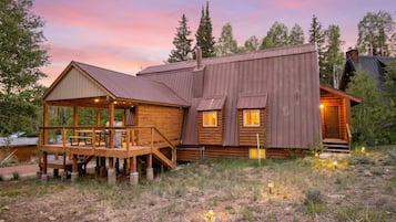 A rustic cabin with a deck, a covered porch, and a large wooden structure.