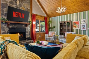 Una sala acogedora con chimenea de piedra, un televisor mostrando 'NETFLIX' y papel tapiz a rayas.