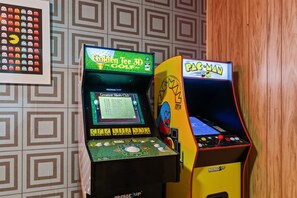 Dos máquinas de arcade, una para Golden Tee 3D Golf y la otra para Pac-Man, con un muro estampado y un cartel de fantasmas al fondo.