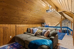 Una stanza accogliente con soffitto in legno, un divano con cuscini, un tavolino e una scala che conduce a un piano superiore.