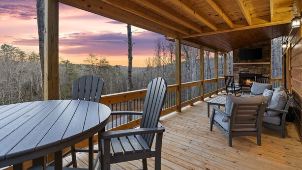 Une terrasse en bois avec une table et des chaises, une cheminée et une vue panoramique sur les arbres et le ciel.
