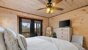 Une chambre dans une cabane en bois, avec un lit, un téléviseur posé sur une commode et un ventilateur de plafond.