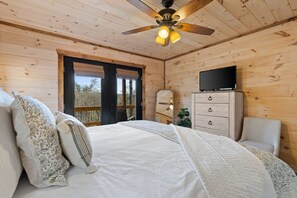 Ein Schlafzimmer einer Holzhütte mit einem Bett, einem Fernseher auf einer Kommode und einem Deckenventilator.