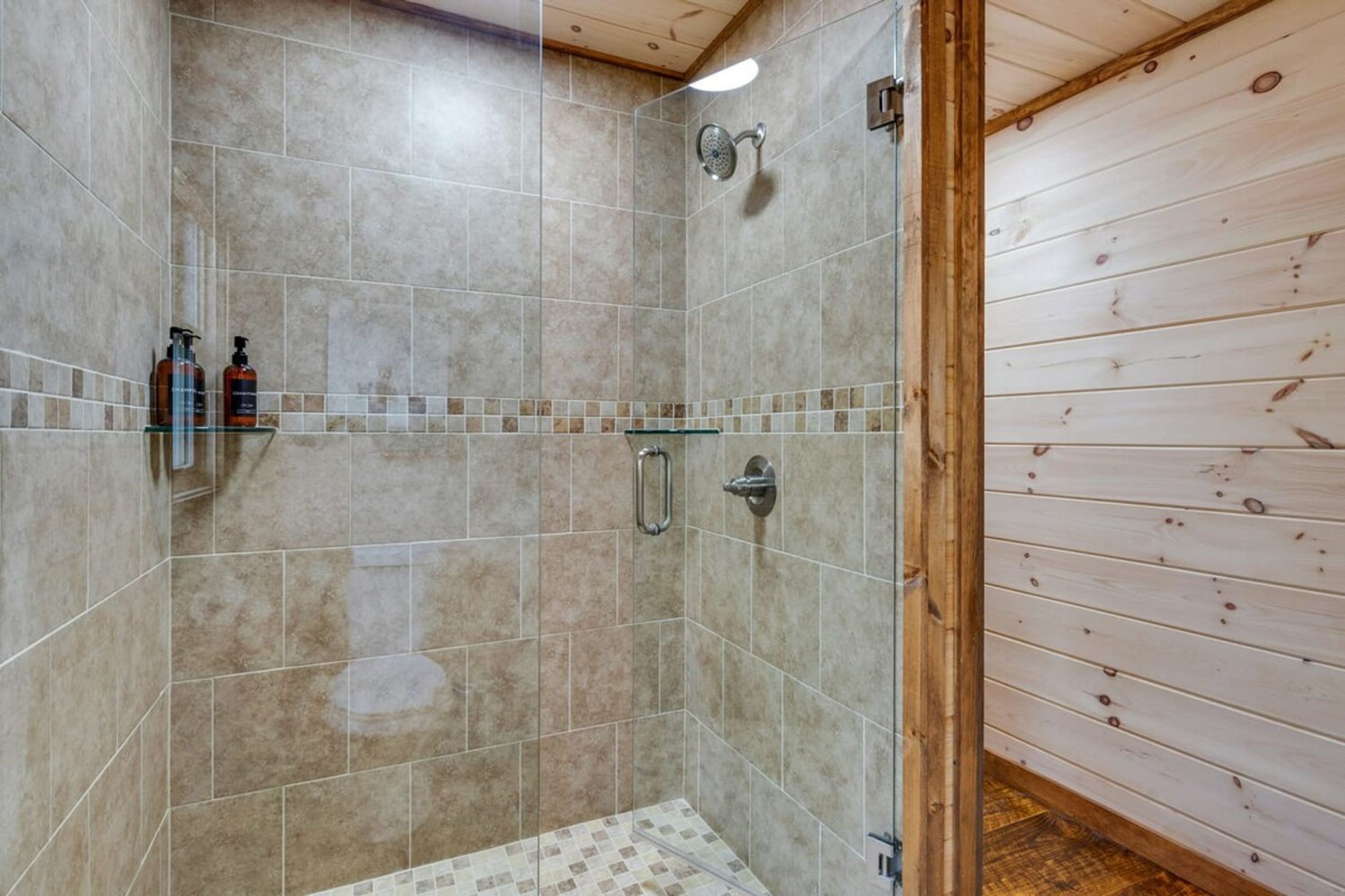 Ducha con paredes de azulejos, puerta de cristal y techo de madera.