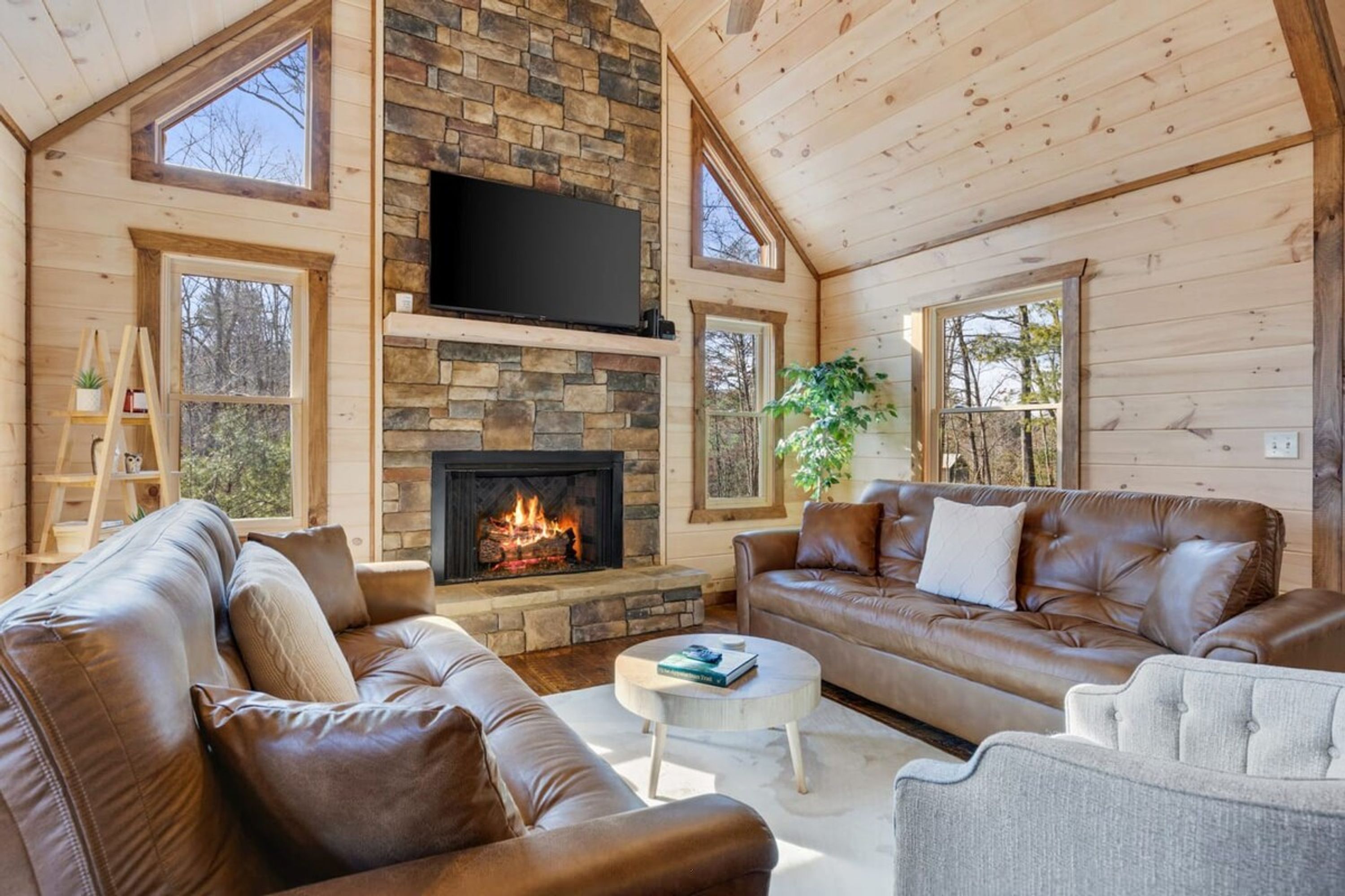 A cozy living room with a stone fireplace, leather sofas, and a flat-screen TV mounted above it.
