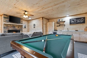 A pool table with billiard balls, a sofa, a fireplace, and a sign for a bar and lounge.