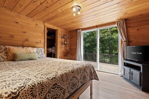 A wooden cabin bedroom with a bed, a TV, and a sliding glass door to a balcony. - Cozy Mountain Escape Hot Tub Fire Pit Views (Blue Ridge)