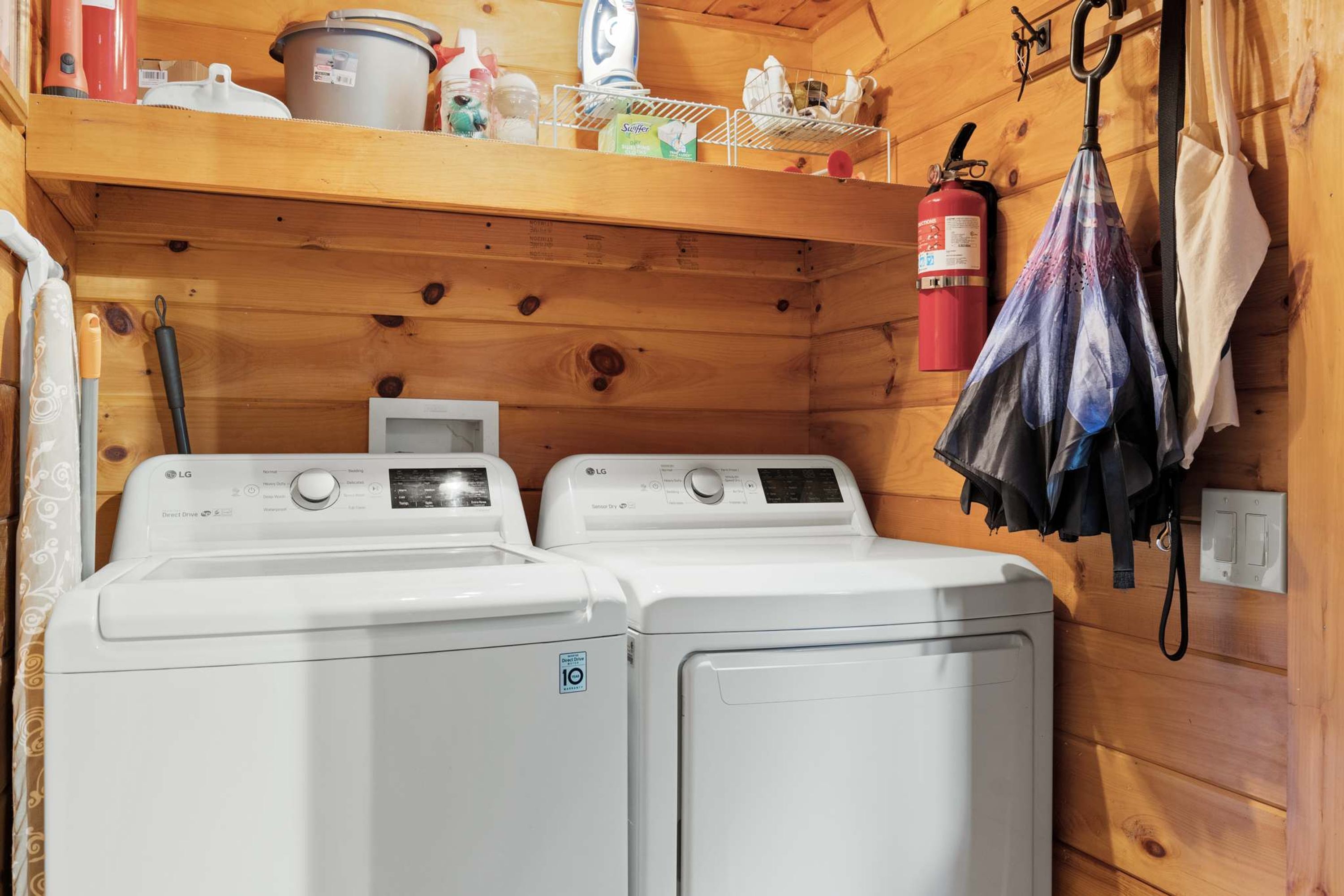 A laundry area with two white LG Direct Drive washing machines, a fire extinguisher, and a shelf with various items.