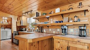 A kitchen with wooden cabinets, a central island, and various appliances including a coffee maker and kettle. - Cozy Mountain Escape Hot Tub Fire Pit Views (Blue Ridge)