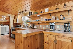 Eine Küche mit Holzschränken, einer zentralen Kochinsel und verschiedenen Geräten, darunter eine Kaffeemaschine und ein Wasserkocher.