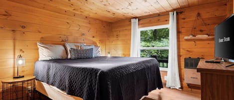 Habitación de cabaña de madera con cama, escritorio, televisión y ventana con cortinas.