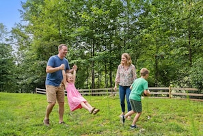 Eine vierköpfige Familie in einer grünen, offenen Landschaft mit Bäumen und einem Holzzaun im Hintergrund.
