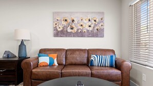 Ein Wohnzimmer mit braunem Ledersofa, einem runden Couchtisch, einer Lampe, einem Gemälde und einem Fenster mit Jalousien.