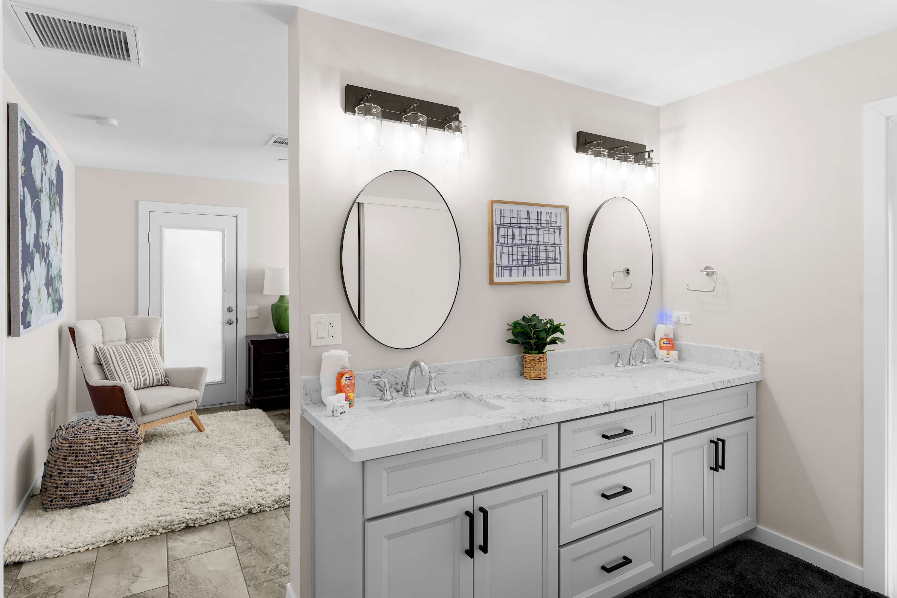 A modern bathroom with a double vanity, a large mirror, and a wall-mounted light fixture.