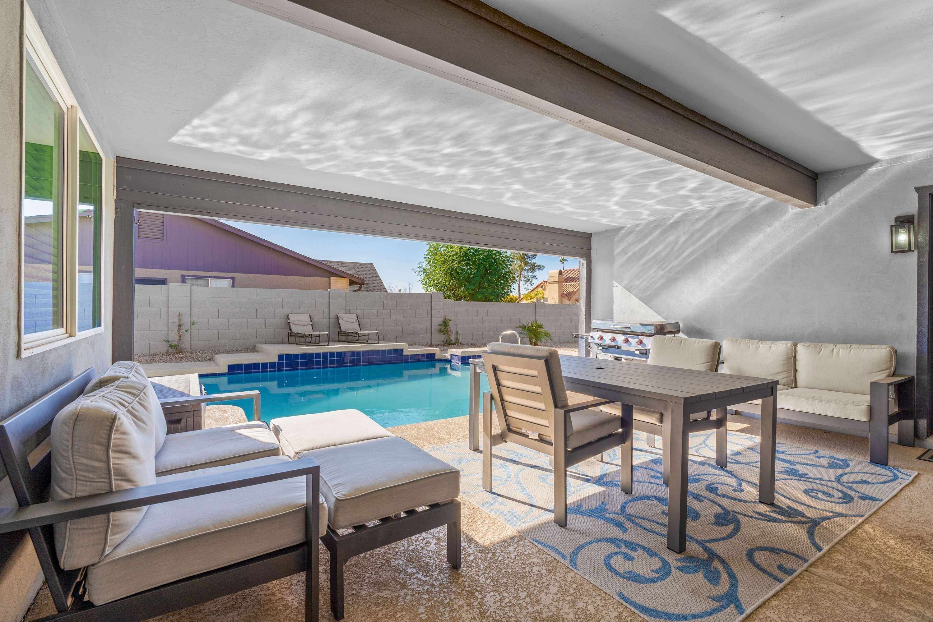 An outdoor patio area with a pool, seating, and a barbecue grill.