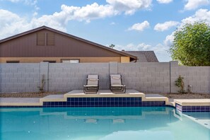 Une piscine avec deux chaises longues, un mur de briques et un bâtiment en arrière-plan.