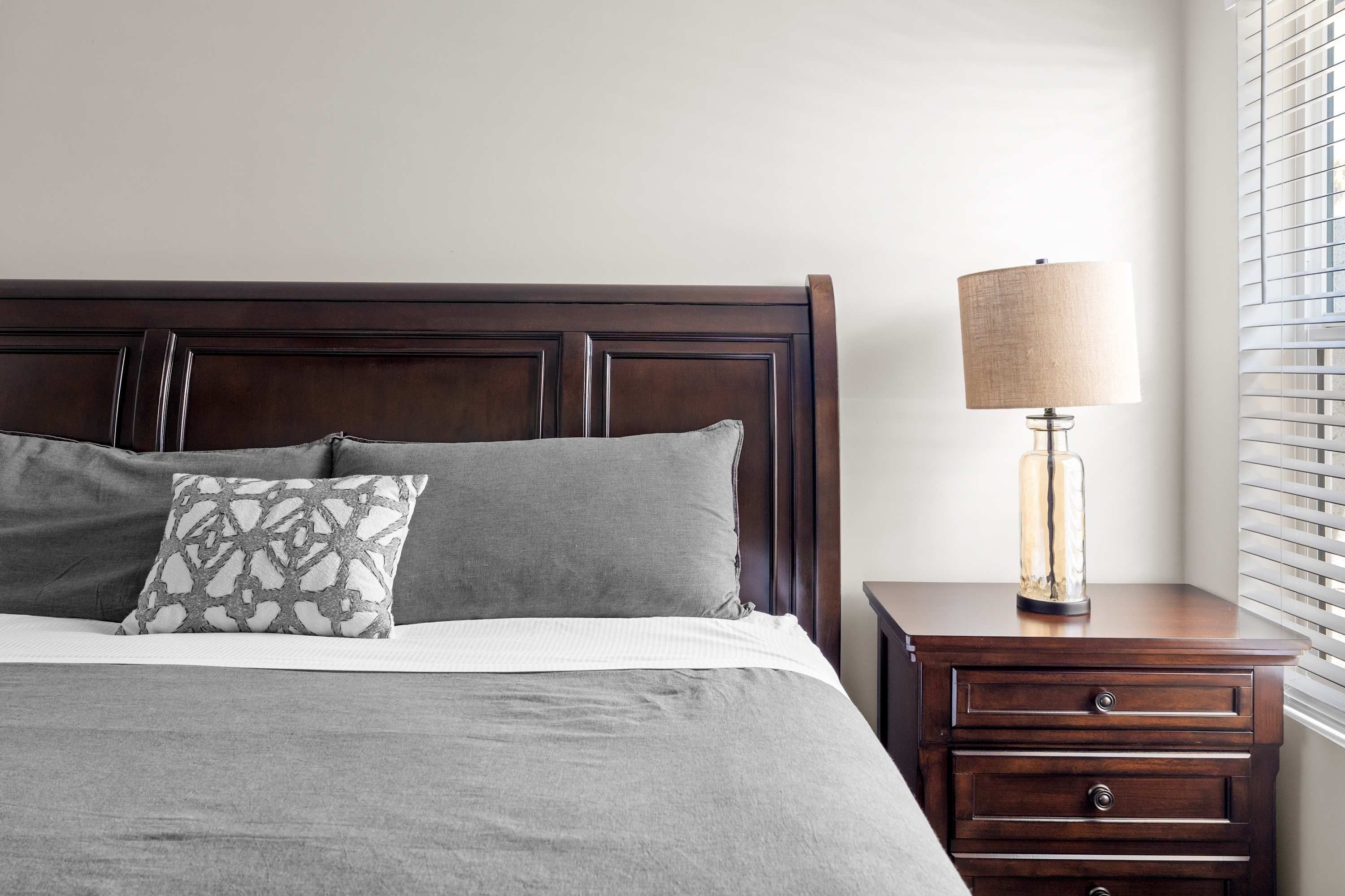 A neatly made bed with a dark headboard, a bedside lamp, and a nightstand with drawers.
