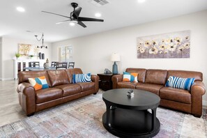 A modern living room with two brown leather sofas, a black coffee table, a ceiling fan, and a dining area in the background. - Poolside Patio Close to Westgate Dog Friendly (Phoenix)