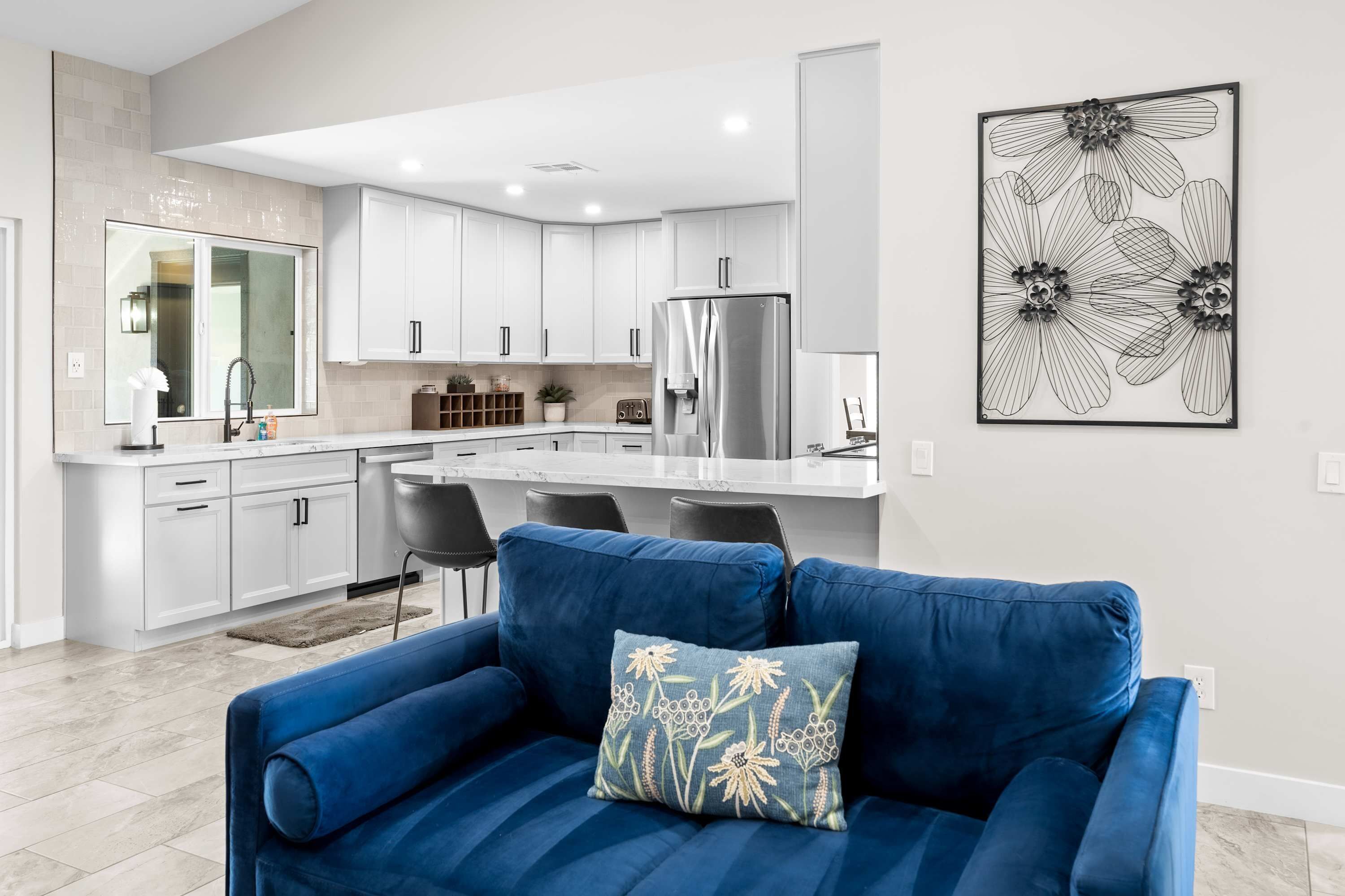A modern kitchen with white cabinets, a stainless steel refrigerator, and a dining area with a blue sofa and a decorative pillow.
