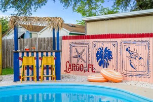 Un patio trasero con piscina, un bar tiki y una pared decorada con motivos náuticos.