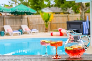 A poolside setting with a clear view of the pool, lounge chairs, and a pitcher of a beverage with fruit slices.