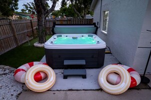 Un jacuzzi con dos anillos inflables, una valla de madera y una casa al fondo.