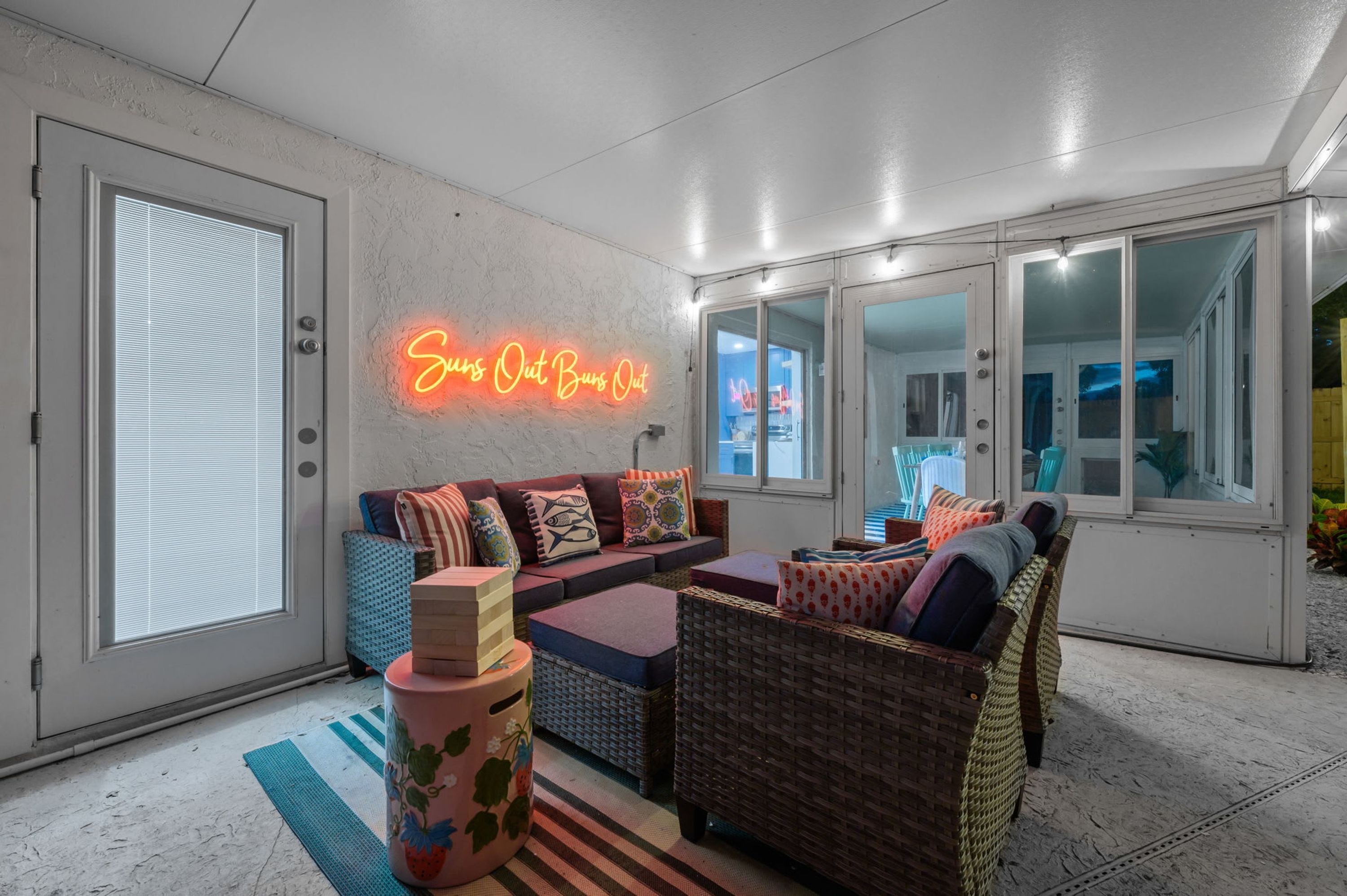 A modern outdoor seating area with a neon sign, wicker furniture, and a view of the city.