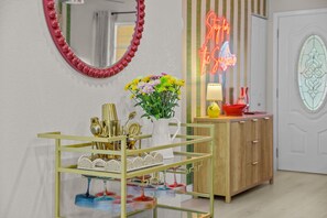 Una habitación con un espejo, un letrero de neón, un florero con flores y una vitrina de vidrio con diversos objetos.