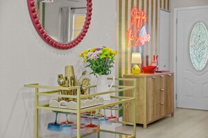 Una habitación con un espejo, un letrero de neón, un florero con flores y una vitrina de vidrio con diversos objetos.