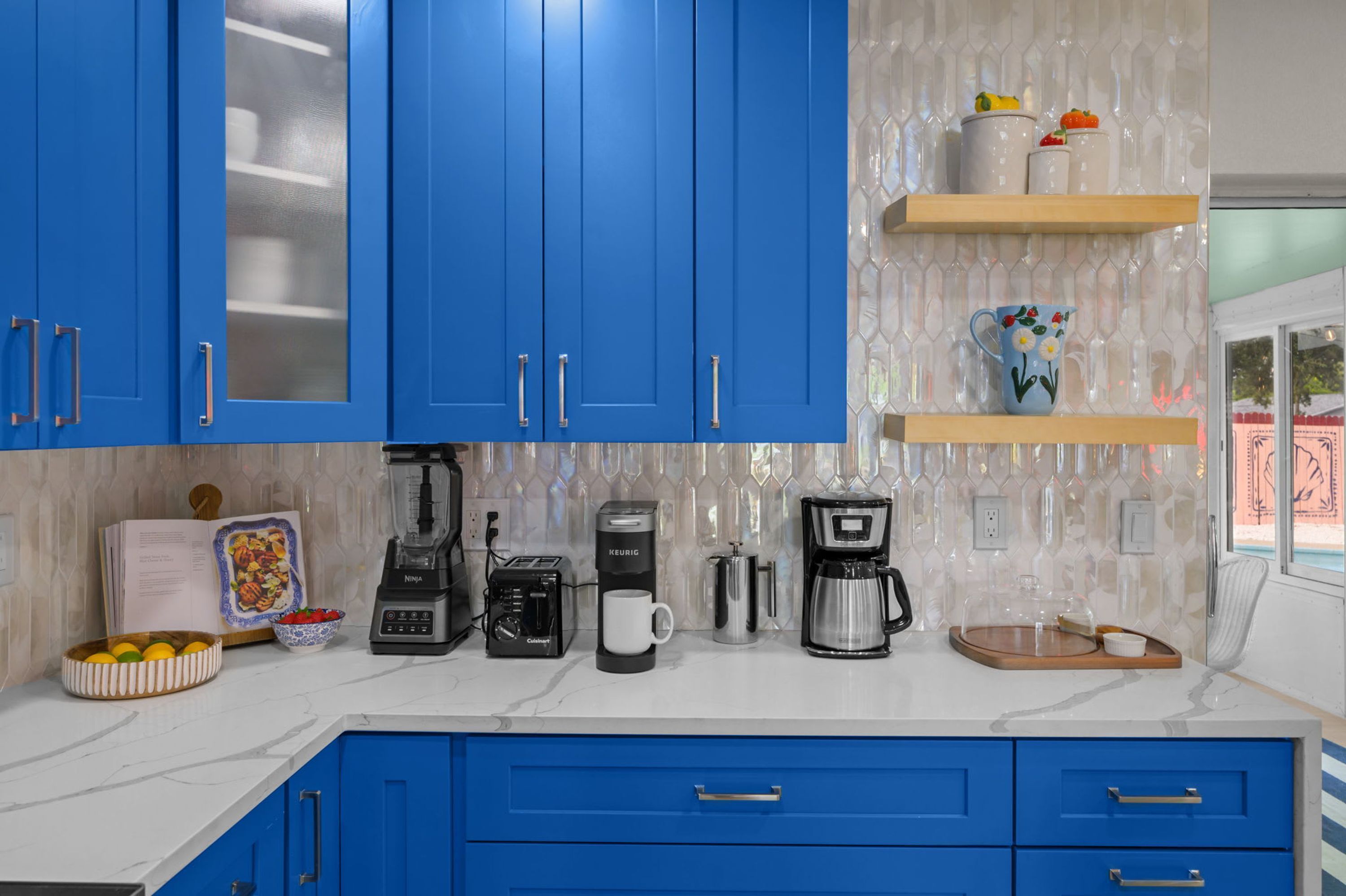A kitchen with blue cabinets, a coffee maker, a toaster, and a bowl of fruit.