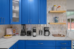 Una cocina con gabinetes azules, una cafetera, un tostador y un bol de fruta.